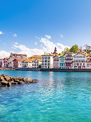 Panoramic view of colorful traditional Basque houses lining the harbor of Saint-Jean-de-Luz under a bright blue sky.