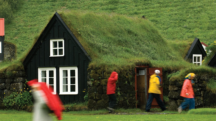 People walking past traditional black wooden turf houses with grass roofs in Skogar, Iceland.