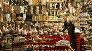 A woman browses a stall filled with ornate metal lamps and handcrafted boxes in the Istanbul Grand Bazaar.