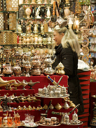 A woman browses a stall filled with ornate metal lamps and handcrafted boxes in the Istanbul Grand Bazaar.