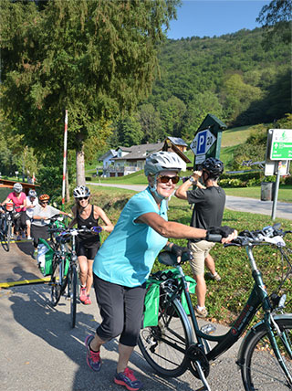 Cyclists wearing helmets push their bikes along a paved path in Schlogen during a biking trip along the Danube River.