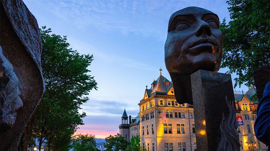 A bronze head sculpture stands before an illuminated historic building during a sunset Quebec Old City walking tour.