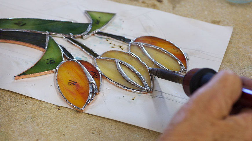 A person uses a soldering iron to join pieces of colored glass for a floral stained glass project at Cedar Lakes, West Virginia.