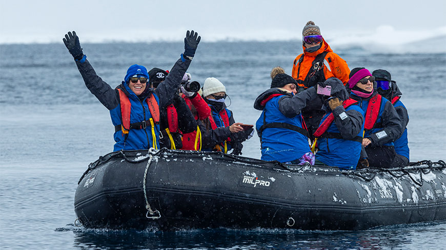 A group of people enjoy Zodiac cruising near Enterprise Island, with one person raising their arms in excitement from the black inflatable boat.