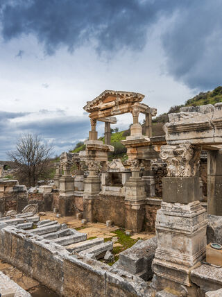 Ancient stone ruins and ornate columns of Ephesus near Kusadasi under a dramatic, cloudy sky.