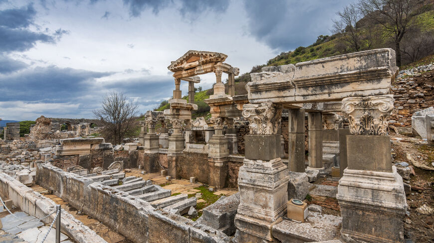 Ancient stone ruins and ornate columns of Ephesus near Kusadasi under a dramatic, cloudy sky.