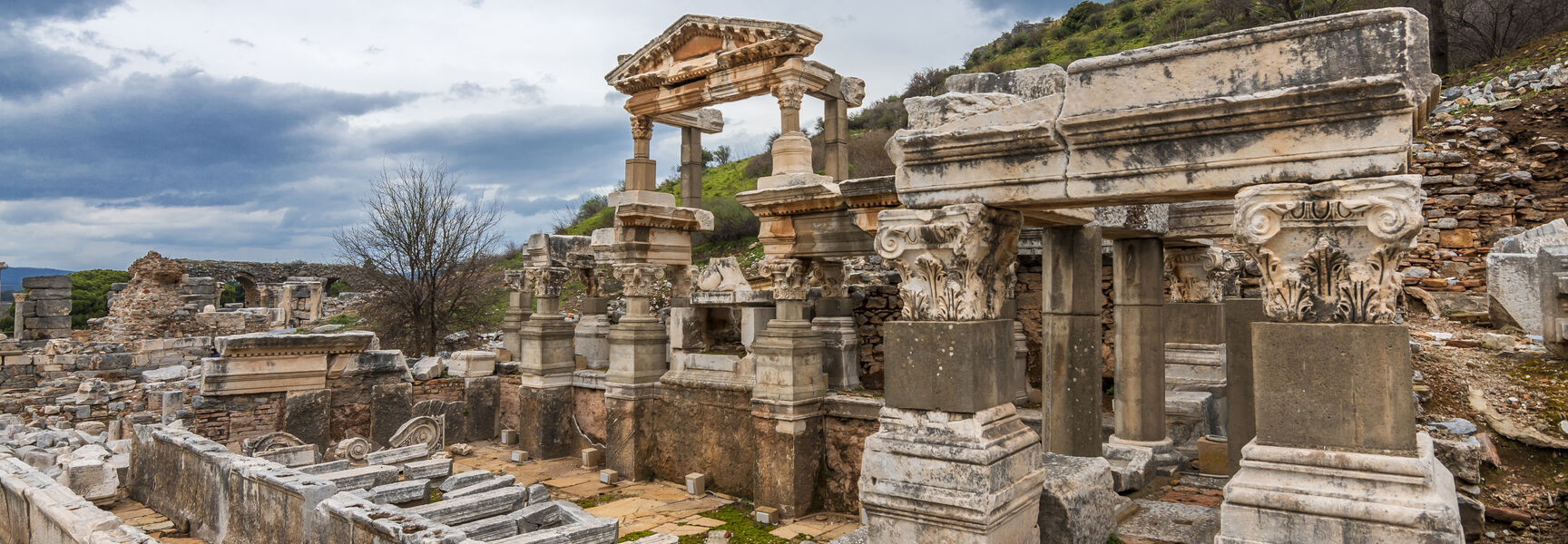 Ancient stone ruins and ornate columns of Ephesus near Kusadasi under a dramatic, cloudy sky.