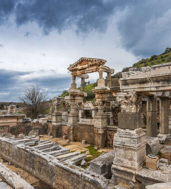 Ancient stone ruins and ornate columns of Ephesus near Kusadasi under a dramatic, cloudy sky.