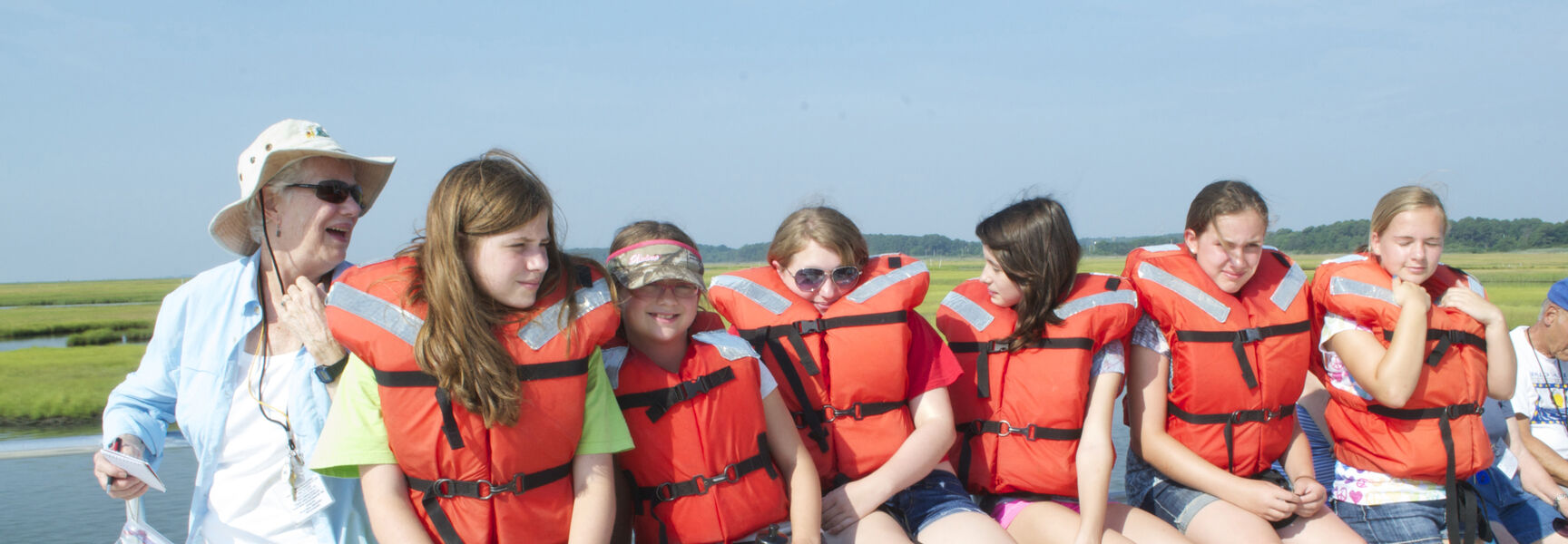A woman and a group of children wearing orange life jackets enjoy a boat ride across Chincoteague Bay in Virginia.