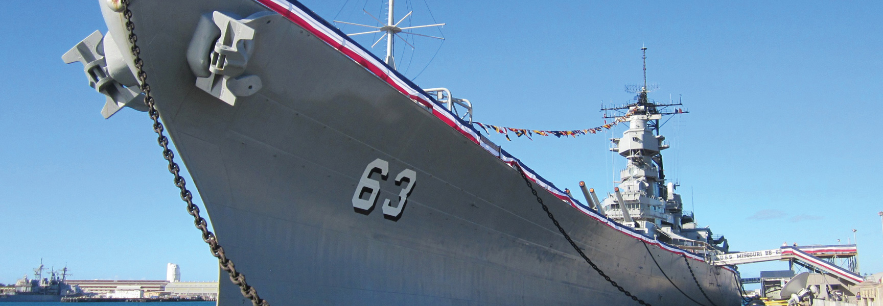 The bow of the USS Missouri battleship docked in Pearl Harbor, Hawaii, under a clear blue sky.