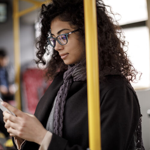 Žena s kovrčavom kosom i naočalama gleda u svoj telefon u autobusu