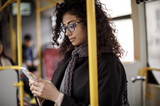 Female with curly hair and glasses looking at her phone on the bus