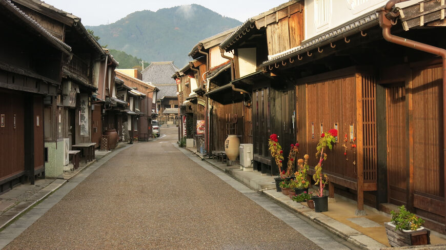A narrow street lined with traditional wooden buildings along the Tokaido Trail in Kameyama, Japan, with a misty mountain visible in the distance.