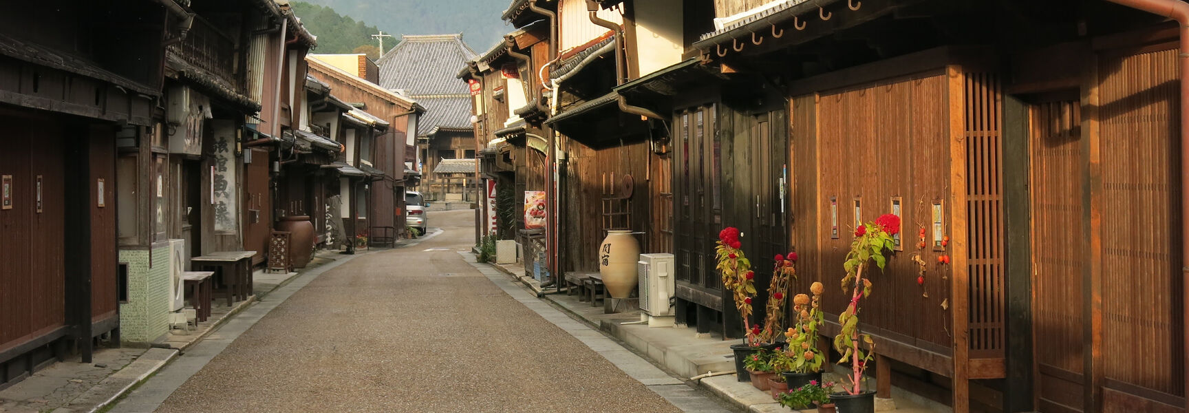 A narrow street lined with traditional wooden buildings along the Tokaido Trail in Kameyama, Japan, with a misty mountain visible in the distance.