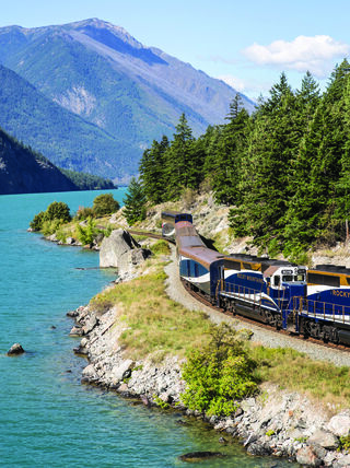 A Rocky Mountaineer train travels along the turquoise shores of a lake through the Canadian Rockies in Alberta and British Columbia.