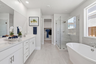 bathroom with white cabinets & counters, tan tile floors, walk-in shower, and window above freestanding tub