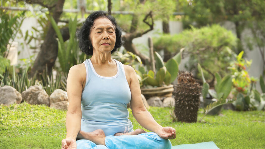 An older woman practices guided meditation in a lush California garden during a rejuvenation retreat for restorative healing and inner peace.