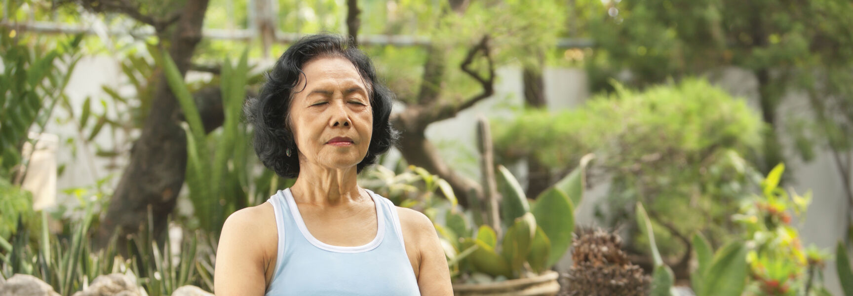 An older woman practices guided meditation in a lush California garden during a rejuvenation retreat for restorative healing and inner peace.