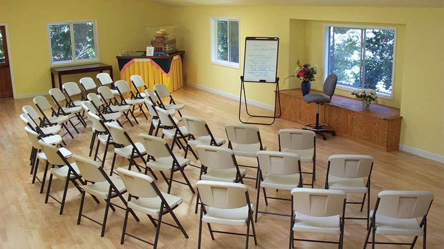 A bright meeting room in California with yellow walls and folding chairs arranged in semi-circles.