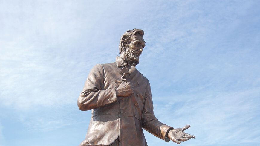 Bronze statue of Abraham Lincoln gesturing with one hand outstretched against a bright blue sky in Illinois.