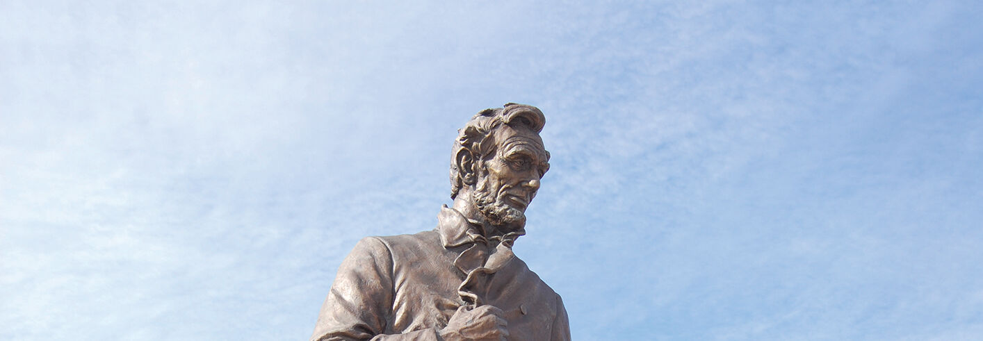 Bronze statue of Abraham Lincoln gesturing with one hand outstretched against a bright blue sky in Illinois.