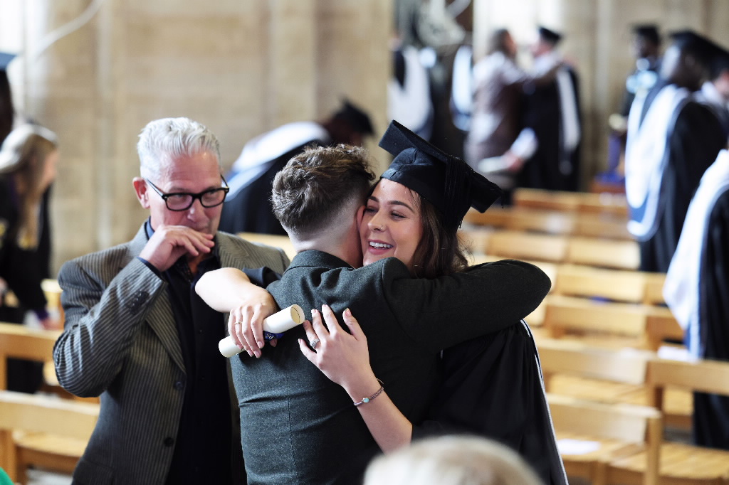 A female graduate, holding her rolled-up scroll, receiving a celebratory hug