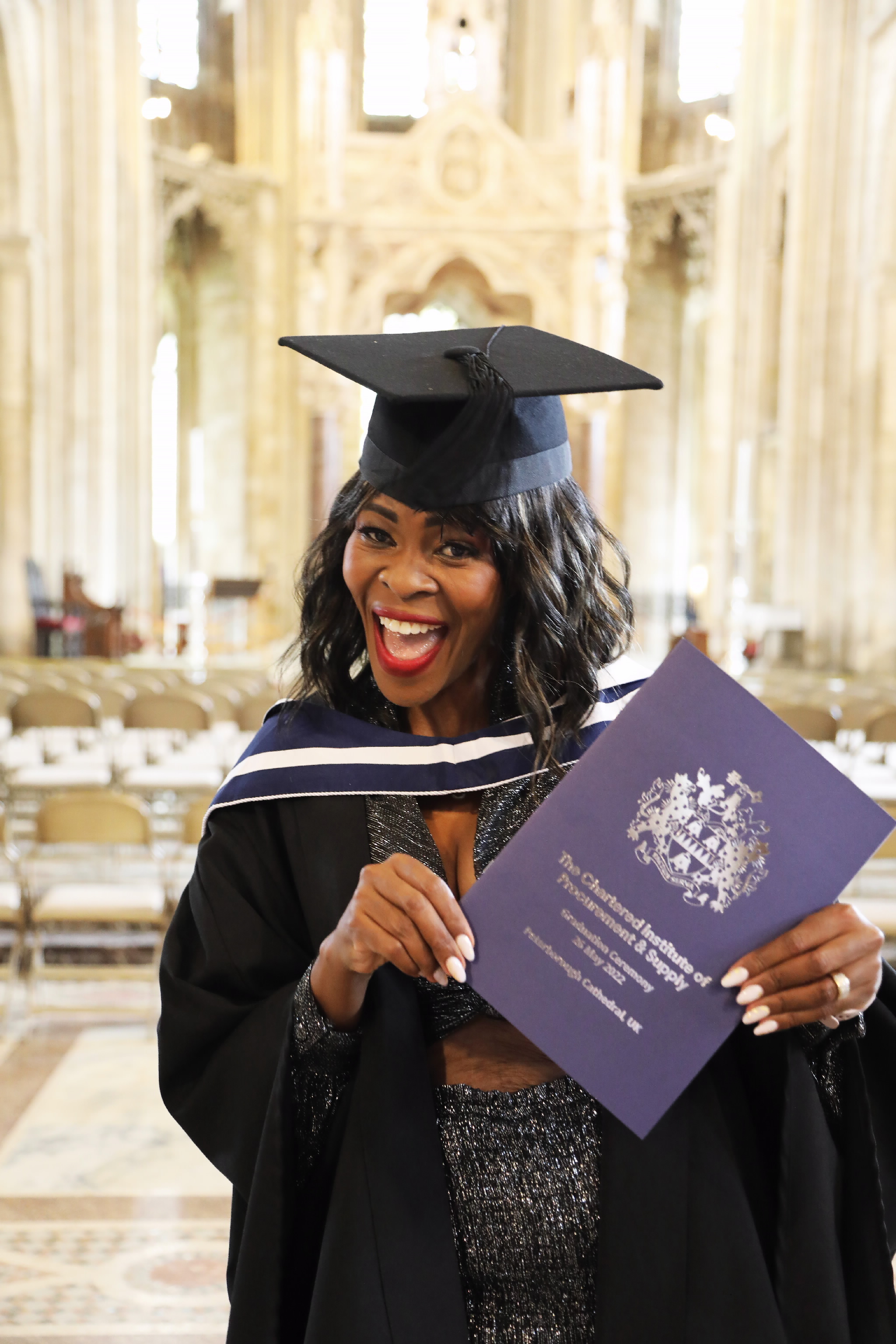 A joyful female graduate holds a diploma folder in a cathedral