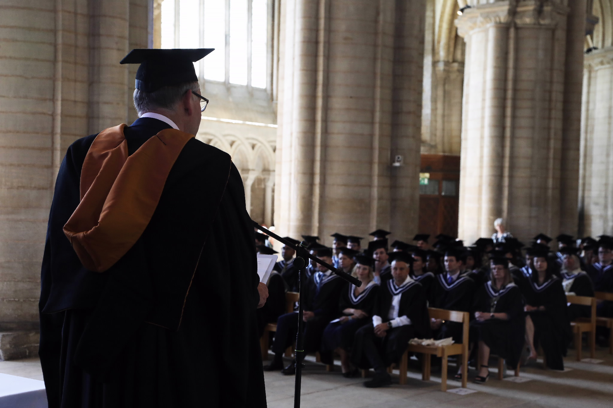 A speaker addresses the seated graduates in a cathedral