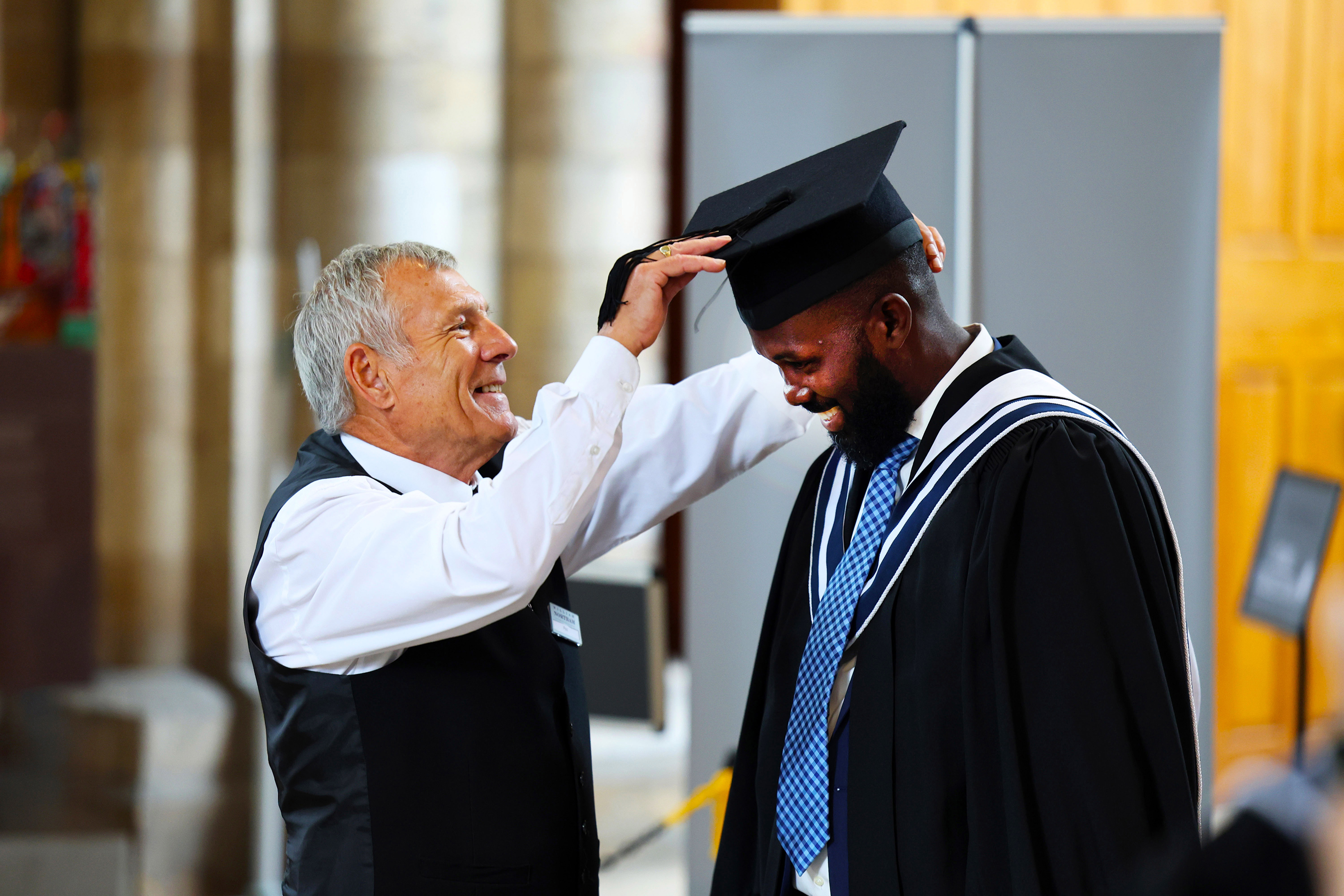 A staff member adjusting a graduate's cap, both smiling