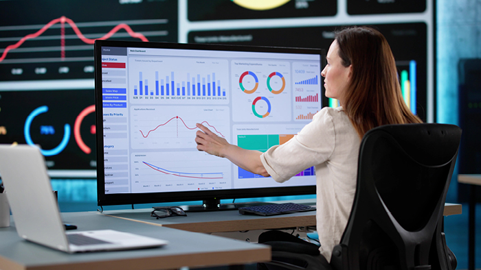 Image of a woman sitting at a desk looking at a live dashboard on a computer screen 