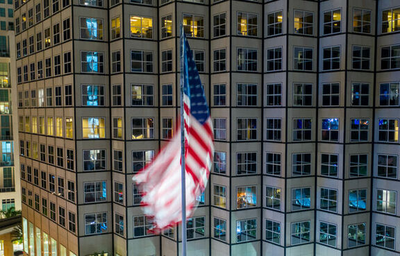American flag displayed at night in front of a tall downtown building 