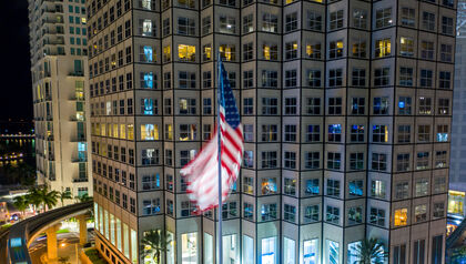 American flag displayed at night in front of a tall downtown building 
