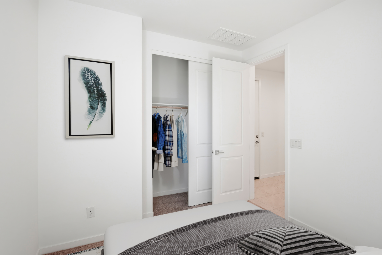 spacious bed with grey bedsheets, a closet with a sliding door, and framed artwork