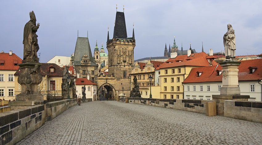 A cobblestone bridge stretches out towards the city, with statues on either side