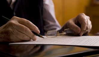 Hands holding a pair of glasses and writing on a piece of paper