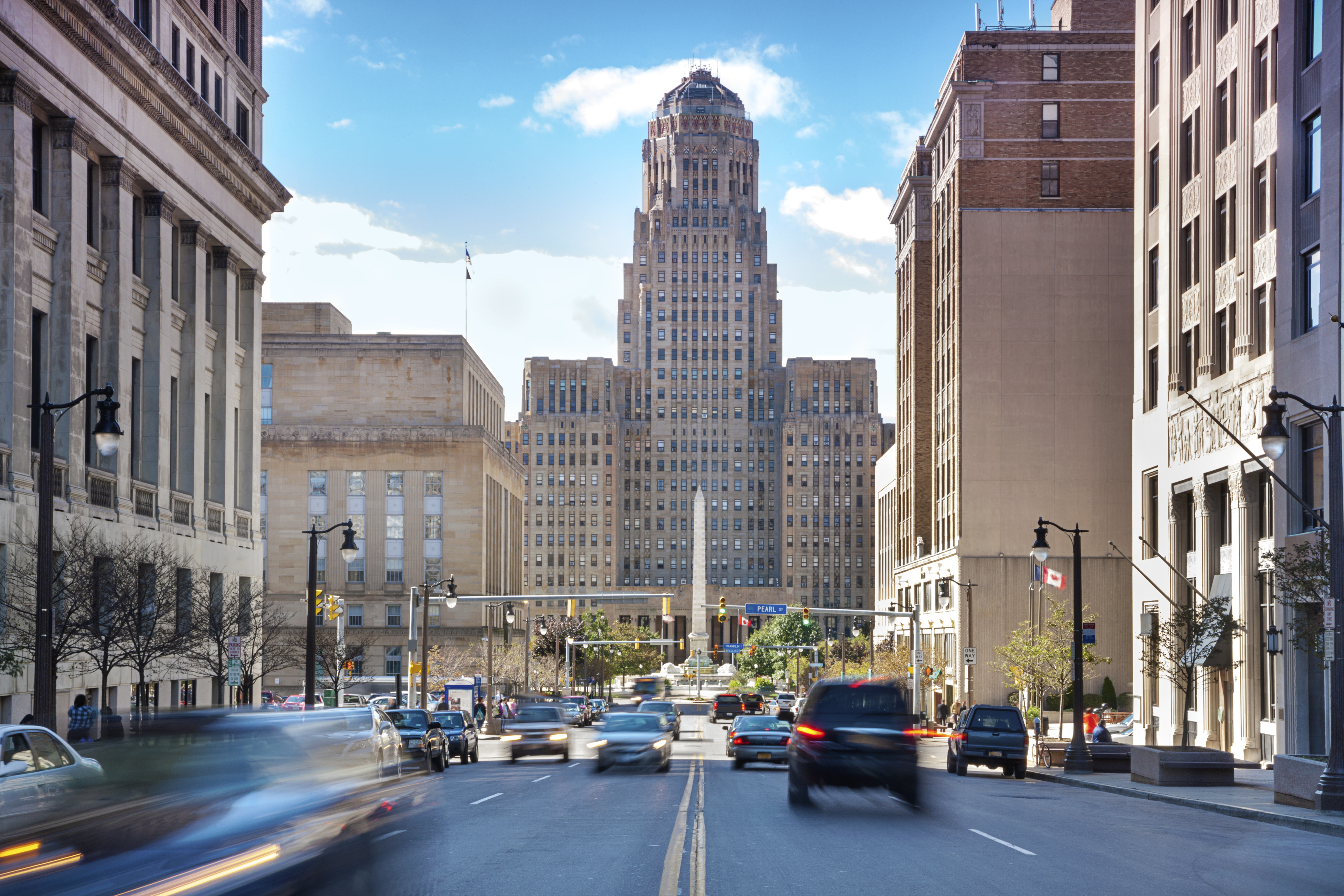 A busy city street with motion-blurred traffic leading to the art deco Buffalo City Hall in downtown Buffalo, New York.