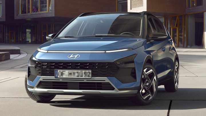 A blue Hyundai Bayon compact SUV parked in front of a modern building, viewed from the front at an angle.