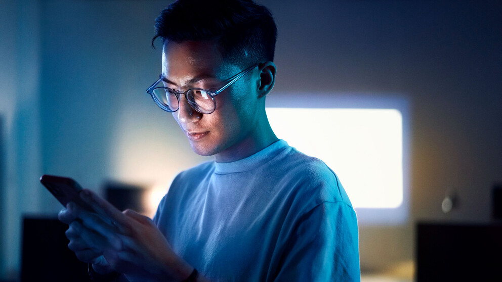 Man looking at his phone at night with a blue light coming from the screen