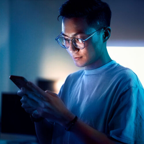 Man looking at his phone at night with a blue light coming from the screen