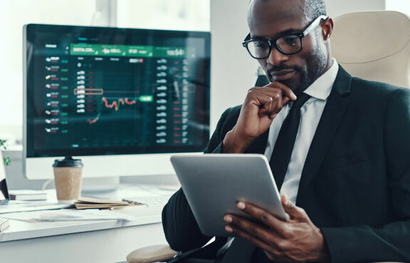 Man in a suit sitting at a desk looking at a tablet