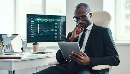 Man in a suit sitting at a desk looking at a tablet