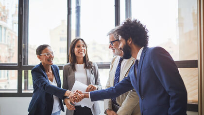 Group of business people in front of a wall of windows shaking hands 