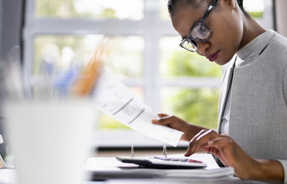 Woman sitting at a desk with computer, papers and calculator