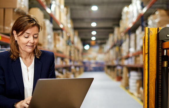 Woman in a warehouse using a laptop on top of boxes
