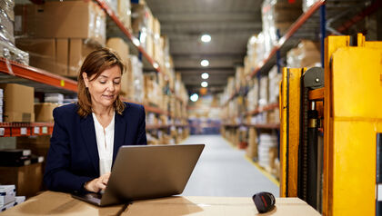 Woman in a warehouse using a laptop on top of boxes