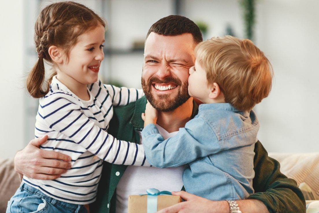 Dad sharing a hug with two children while holding a Father’s Day gift.