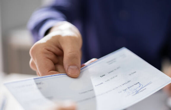 Man handing someone a paper check while seated at a desk