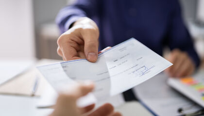 Man handing someone a paper check while seated at a desk