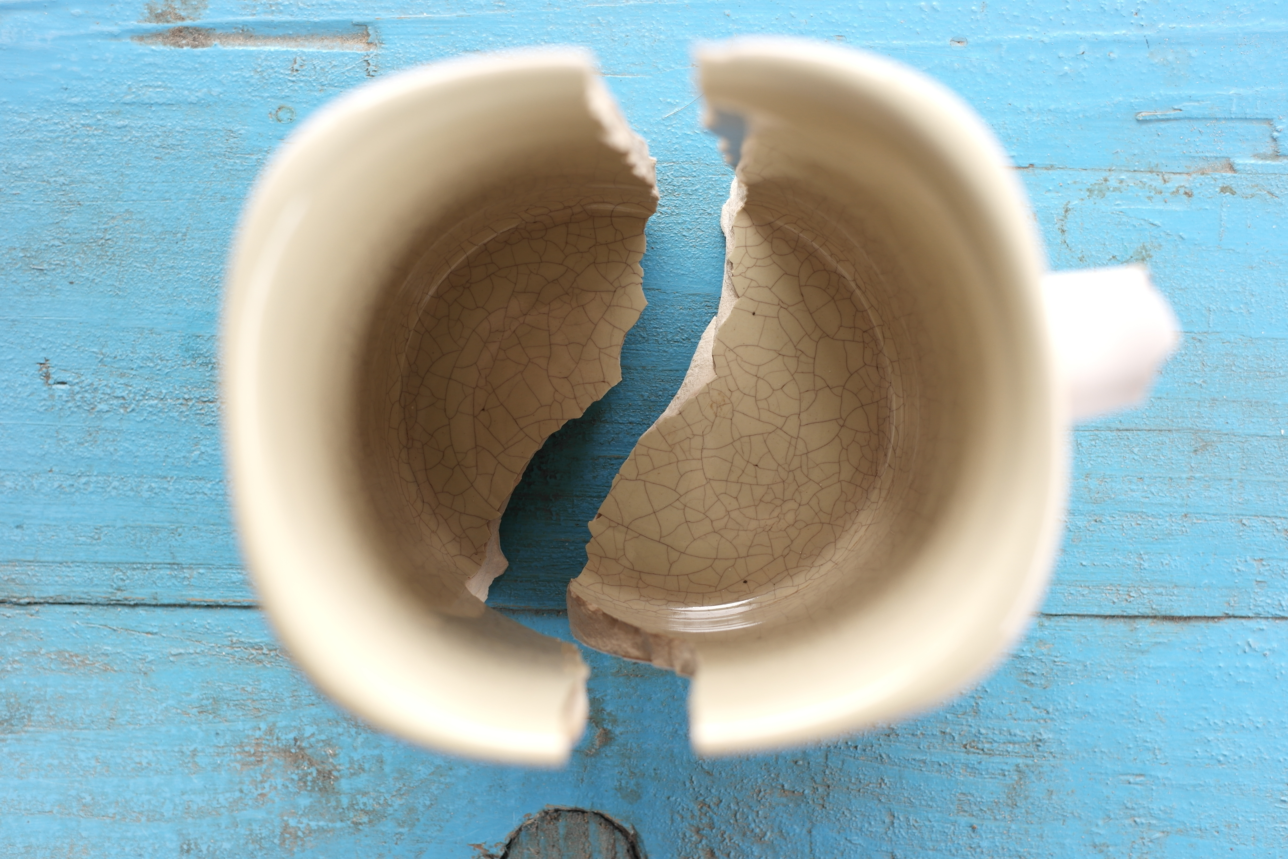 Cracked ceramic mug on blue background