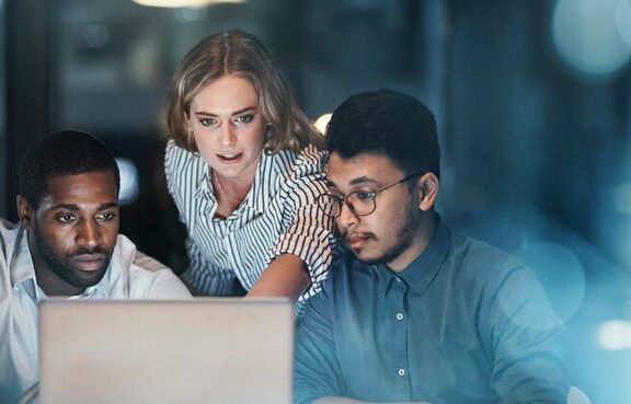 Three young businesspeople working together on laptop at night